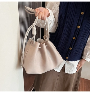 Detail of cream drawstring bucket bag with litchi grain texture and knotted rope strap