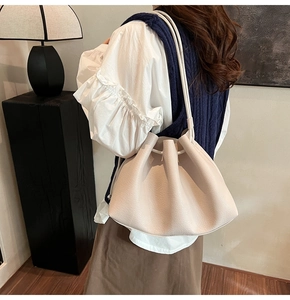 Detail of minimalist cream bucket bag with drawstring closure and litchi grain texture