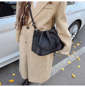 Detailed view of black litchi grain leather bucket bag on camel cashmere coat