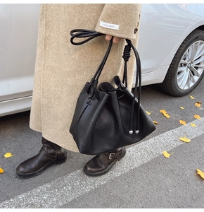 Detail of a black leather bucket bag with drawstring closure shown on a model