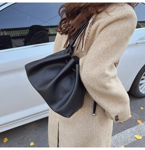 Close-up of black lychee-grain leather bucket bag worn with a beige autumn coat