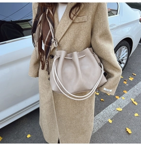 Detail of beige lychee pattern bucket bag with drawstring and woven knot shoulder strap
