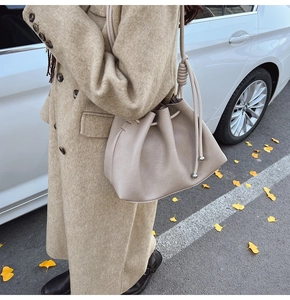Detailed close-up of beige lychee textured bucket bag with silver drawstring accents