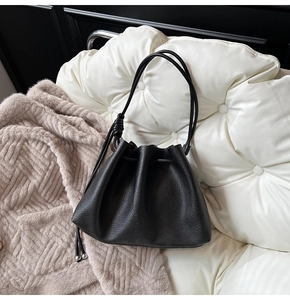 Detail of black drawstring bucket bag with litchi leather texture and knot strap