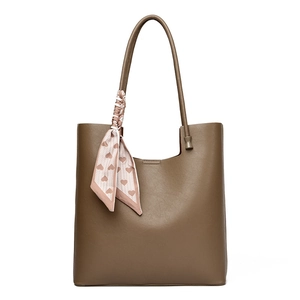 Brown leather tote bag with a pink heart silk scarf on the strap in a clean studio view