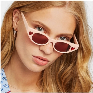 Pink cat eye sunglasses with red heart details worn by a model in a close-up fashion shot