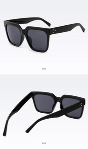 Detail view of black square sunglasses featuring gold rivet accents on the temples