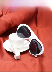 Close-up of stylish oversized white sunglasses on orange silk fabric next to a white cup