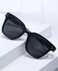 Close-up of square black sunglasses with silver rivet details on geometric white display