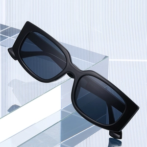 Classic square black sunglasses with thick frames and dark lenses on a modern glass stand