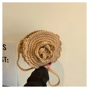Detail of handmade woven round bag featuring large floral decoration and braided shoulder strap