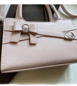 Close-up of light pink handbag with decorative bow, silver buckles and cross straps