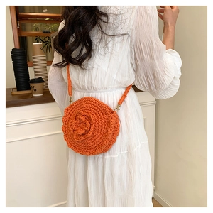 Detail of a handmade orange crochet round bag with 3D floral accent and woven strap