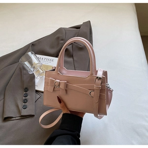 Pink faux leather tote bag with bow detail and adjustable strap held by hand