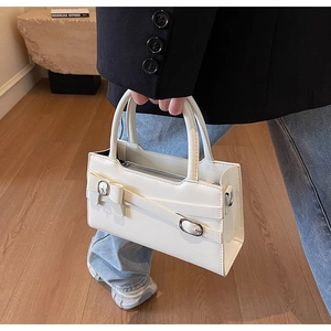 Detailed view of white rectangular tote with silver buckle and cross-strap decorative accents