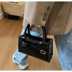 Close-up of black glossy leather tote with silver buckle and bow detail on model