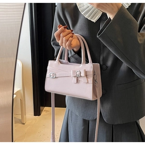 Detail of light pink crossbody bag featuring a decorative bow and silver buckle clasp