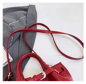 Detail of red leather handbag showing dual handles and adjustable silver shoulder strap