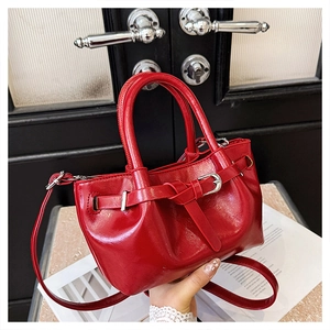 Close-up of red glossy leather handbag with belt buckle detail and detachable strap