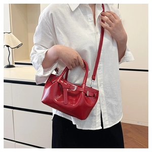 Detail view of a glossy red patent leather handbag with silver buckles and a thin shoulder strap