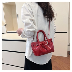 Red glossy patent leather handbag with dual handles and adjustable shoulder strap worn by model