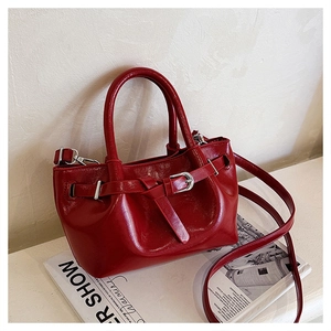 Detail of red glossy leather handbag with silver metal buckles and adjustable strap