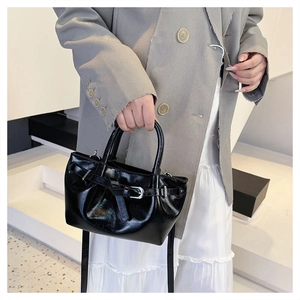 Close-up of black glossy handbag with pleated details and silver metal buckle