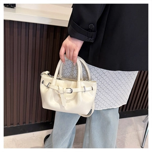 Detail of cream drawstring handbag featuring metal buckle strap and dual round handles