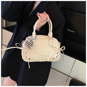 Détail du sac Boston crème avec lanières à nœud et breloque en cœur dans un décor moderne