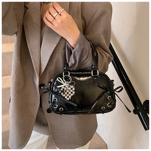 Détail d'un sac Boston en cuir verni noir avec nœud en ruban et breloque en cœur