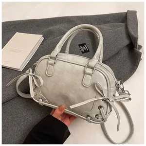 Détail du sac Boston gris clair montrant la texture du cuir et les nœuds de ruban chic