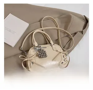 Détail du sac Boston crème avec nœud, pendentif en cœur et finition en similicuir