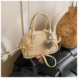 Détail du sac Boston crème avec nœud décoratif et pendentif cœur argenté