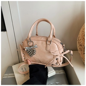 Sac Boston rose avec nœud décoratif et breloque cœur en métal sur une valise argentée