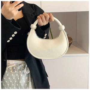 Detail der cremefarbenen Halbmond-Handtasche mit rundem Griff und kugelförmigen Akzenten