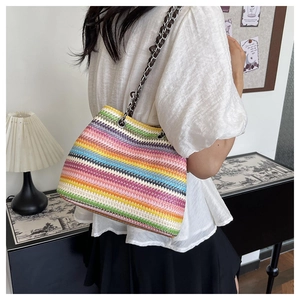 Rainbow striped woven crossbody bag with metal chain strap worn at a 45-degree angle