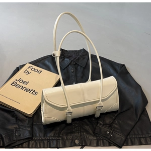 Detail of minimalist cream baguette bag with dual shoulder straps on black leather backdrop