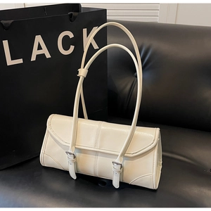 Detail of cream white baguette bag with metallic buckles on a black leather background