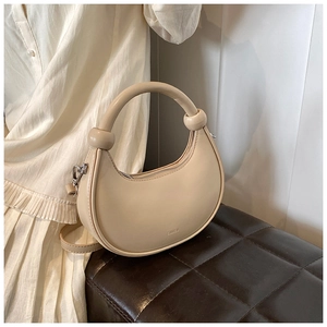 Detail einer beige Halbmond-Handtasche mit rundem Griff auf einem Lederhocker