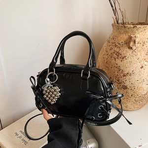 Sac Boston en cuir noir brillant avec nœud et pendentif cœur sur fond blanc minimaliste