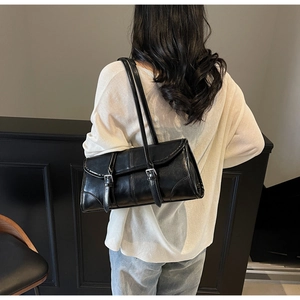Detail of black rectangular leather baguette bag with dual shoulder straps and buckles