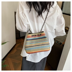 Detail of colorful woven bucket bag with metal chain strap worn by a model in a home setting