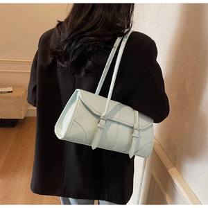 Detail of light blue leather baguette bag with dual buckles on a model's shoulder