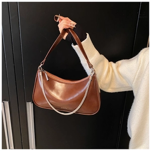 Close-up of brown glossy leather crescent bag with silver chain detail and sleek zipper