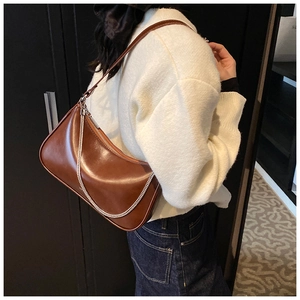 Brown faux leather hobo bag with silver chain detail on a white sweater model