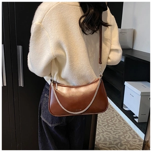 Rear view of a model wearing a brown leather hobo bag with silver chain details