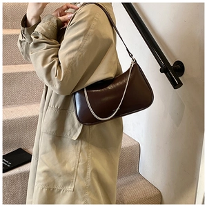 Detail of dark brown leather underarm bag with silver chain worn with a beige trench coat