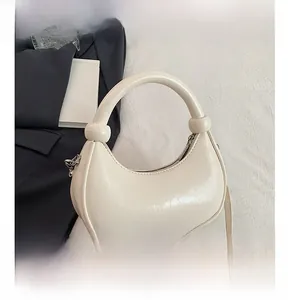 Close-up of cream beige semi-circle hobo bag featuring a knotted handle and glossy leather finish