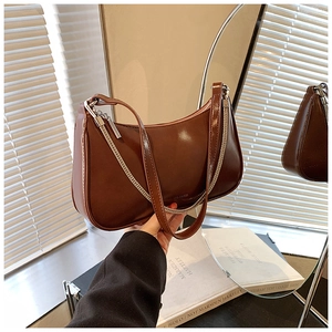 Detail of a brown glossy leather hobo bag with a silver chain strap and zipper closure
