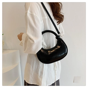 Detail of black crescent handbag featuring glossy wrinkled texture and silver hardware